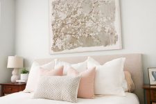 a chic feminine bedroom with grey walls, an upholstered bed, neutral and pastel bedding, wooden nightstands and a floral artwork