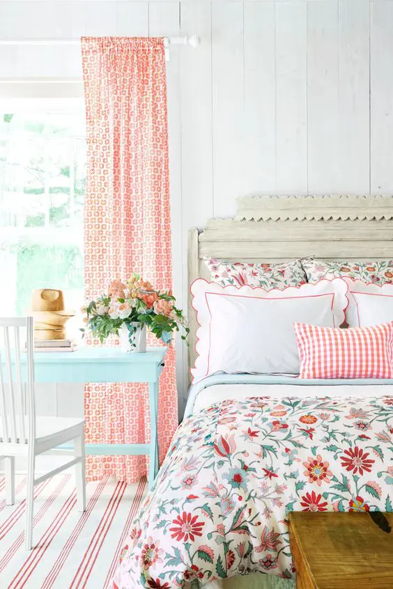 a colorful vintage bedroom with elegant vintage furniture, floral bedding, printed curtains, a blue table and bold blooms