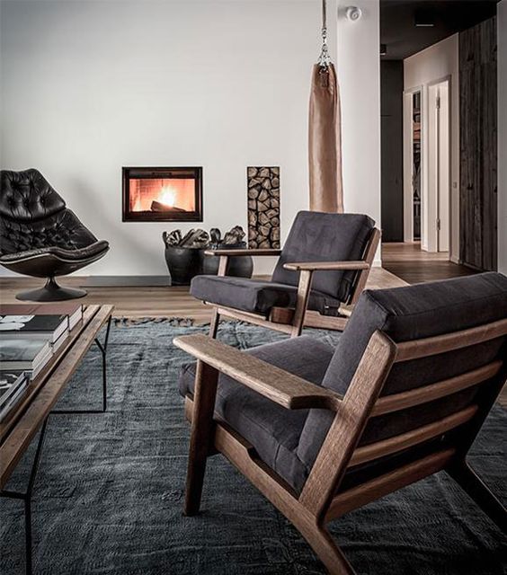 A contemporary living room with dark furniture, a built in fireplace and firewood storage, a dark rug and a coffee table