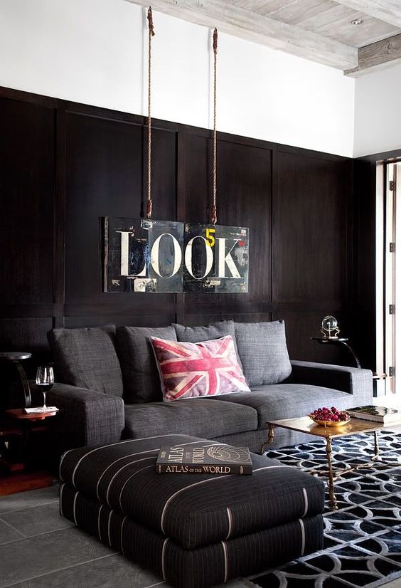a contemporary masculine living room with dark walls, upholstered furniture, a printed rug, a metal table and a sign