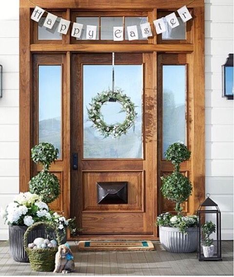 a cozy Easter porch with a bunting, greenery topiaries, blooms in baskets and lanterns and eggs in moss baskets