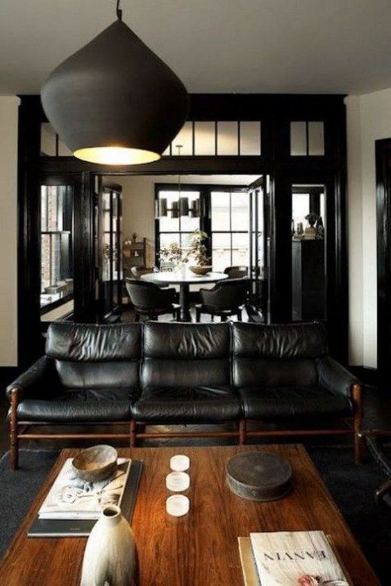 a cozy dark manly room with a black elather sofa, a wooden coffee table, a matte black pendant lamp and candles