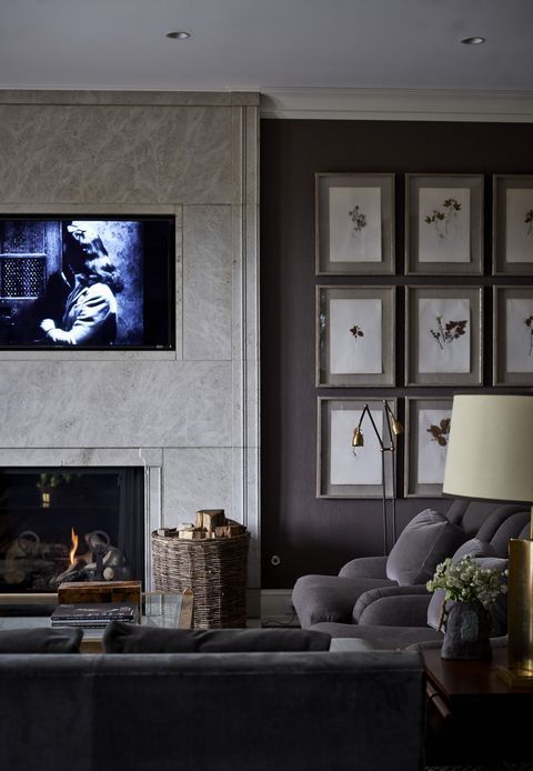 a cozy masculine livign room with a gallery wall, grey furniture, a basket with firewood, a fireplace and some lamps