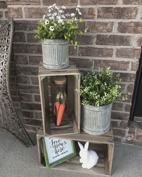 a cute rustic spring decoration of crates, a bunny, a sign, some potted greenery and flwoers and carrots in a jar