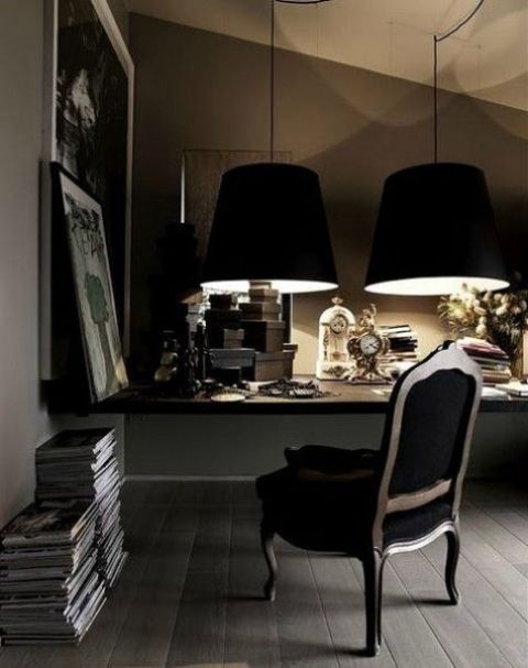 a dramatic masculine home office with a floating desk, a refined chair, large black lamps and stacks of books