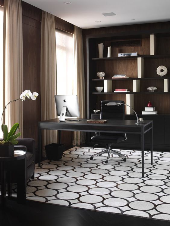 a laconic home office with open shelving, an elegant desk, a printed rug, neutral curtains and a potted orchid