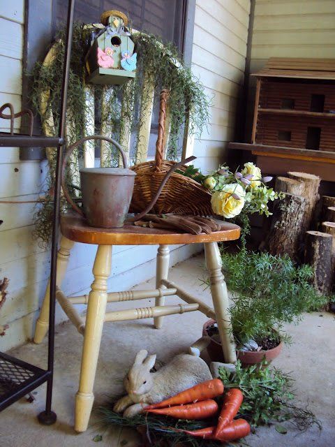 a lovely porch decoration with much greenery, carrots, bird houses and a basket with flowers