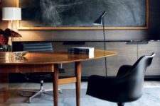 a luxurious home office with an oval wooden desk, black leather chairs and an oversized dark artwork