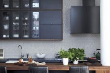a masculine kitchen with graphite grey cabinets, a wooden kitchen island, black leather stools and a black hood