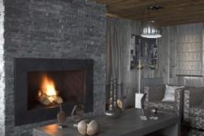 a masculine living room with a stone clad fireplace, wooden tables, a faux fur rug, upholstered furniture and lamps