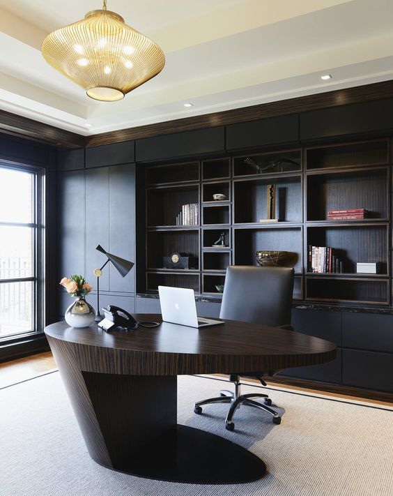 a minimalist and refined home office with a black built-in shelving unit, a sculptural oval desk of rich stained wood, a bold chandelier