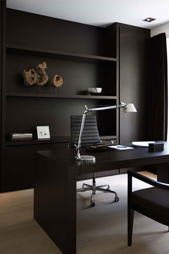 a minimalist home office with matte black walls and built-in shelves, a black desk and comfortable chairs