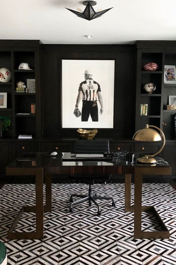 A modenr moody masculine home office with blakc built in shelves, a dark stained desk, a sport themed artwork plus shiny metal accents