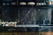 a moody and chic masculine kitchen with a black marble backsplash and countertops, rich-stained wooden furniture