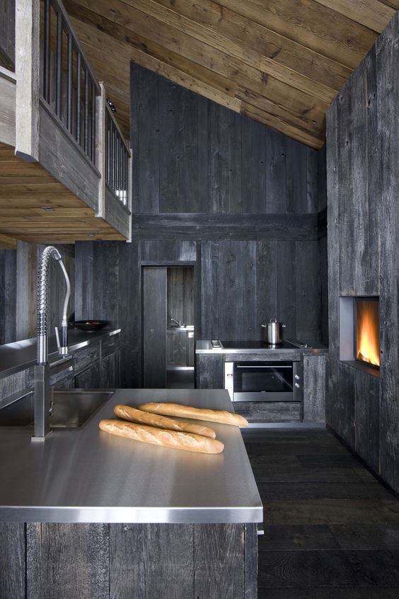 a moody and rough grey kitchen of wood with metal countertops, a hearth and wooden walls for a rustic feel