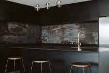 a moody black kitchen with sleek cabinets, a rusty metal backsplash, pendant lamps and tall stools