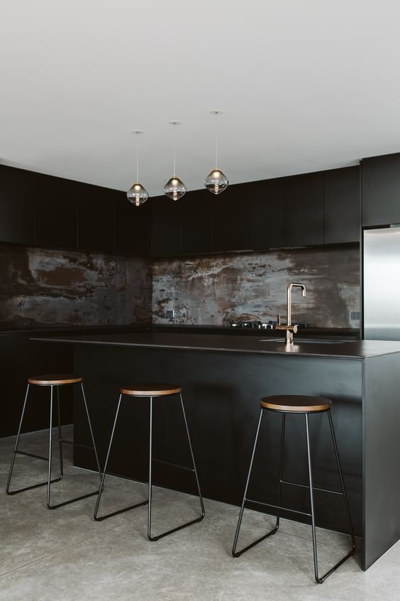 a moody black kitchen with sleek cabinets, a rusty metal backsplash, pendant lamps and tall stools
