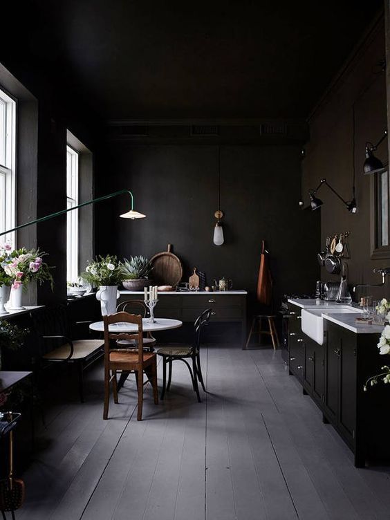 a moody vintage kitchen with white countertops, wall lamps and floral arrangements