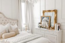 a neutral Versaille-inspired bedroom with refined furniture, a crystal chandelier, gold framed art and mirrors and layered bedding
