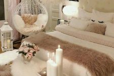 a neutral and blush feminine bedroom with a white upholstered bed, a furry bench, a suspended chair and a feather chandelier
