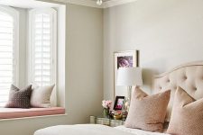 a neutral and pastel feminine bedroom with an upholstered bed, a crystal chandelier, blush and other pillows and a metallic nightstand