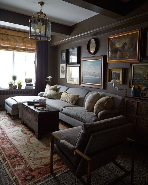 a refined dark living room with grey walls, grey furniture, printed textiles, a vintage lamp and a gallery wall
