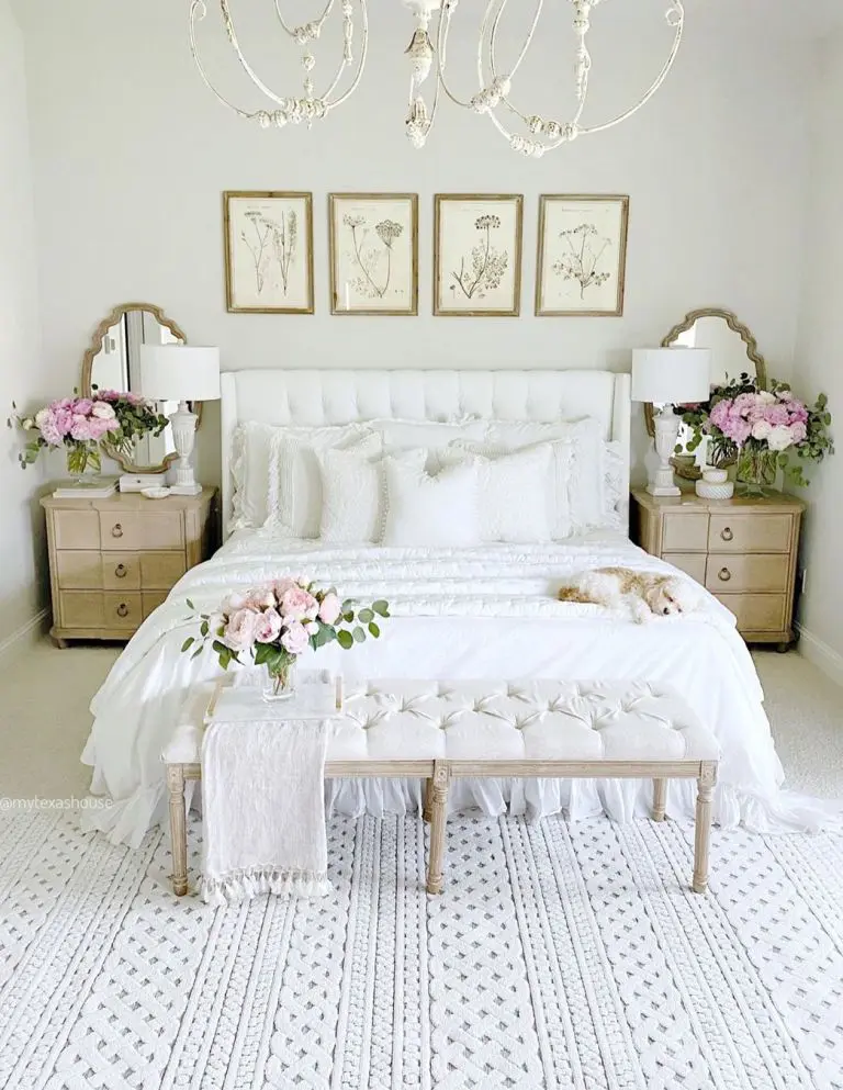 a shabby chic feminine bedroom with a white bed and bench, botanical artworks, wooden nightstands, a chic chandelier and blooms