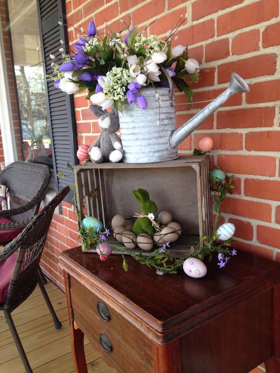 a simple Easter decoration of a crate with colorful eggs, a watering can with a spring bloom arrangement and bunnies