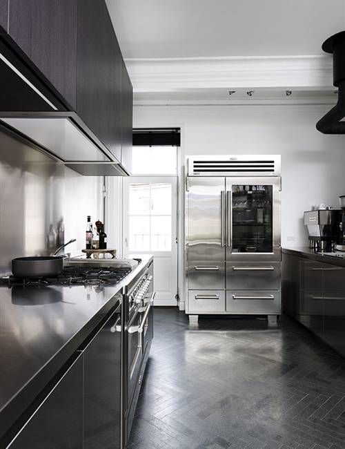 a sleek black kitchen with metal countertops, a large metal hearth and a sleek metal backsplash