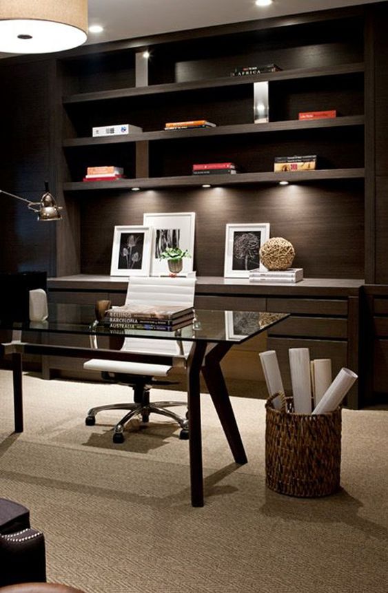 a stylish contemporary home office with a glass desk and a dark stained built-in shelving unit plus drawers and lamps