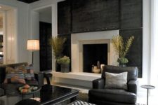 a stylish dark living room with a dark wall, a fireplace, dark furniture, a grey rug and a sleek black table