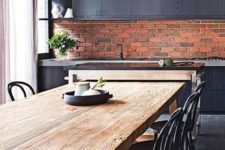 a stylish masculine kitchen with a red brick backsplash and black cabinets and pendant lamps