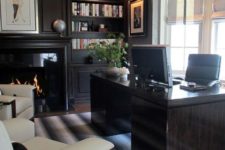 a super chic masculine home office with dark built-in shelves, a fireplace, a dark desk and creamy upholstered chairs