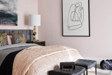a super stylish feminine bedroom with light pink walls, a grey bed, black woven stools, a statement artwork and touches of gold