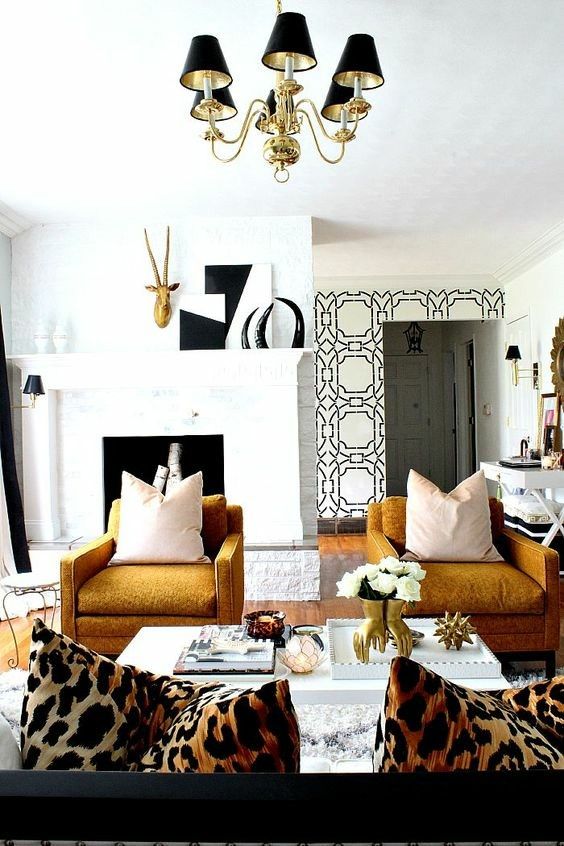 an elegant living room with a non-working fireplace, mustard chairs, a lovely gold and black chandelier and a sofa with leopard print pillows