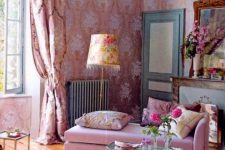 an exquisite feminine living room with beautiful pink wallpaper, a pink daybed, a chic chandelier, pink printed curtains and a faux fireplace