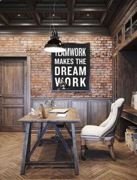 an industrial home office with brick walls, a built-in shelving unit, a wooden desk and a comfy upholstered chair