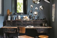 an industrial home office with grey walls, an arrangement of mirrors, a shabby chic wooden desk and industrial chairs