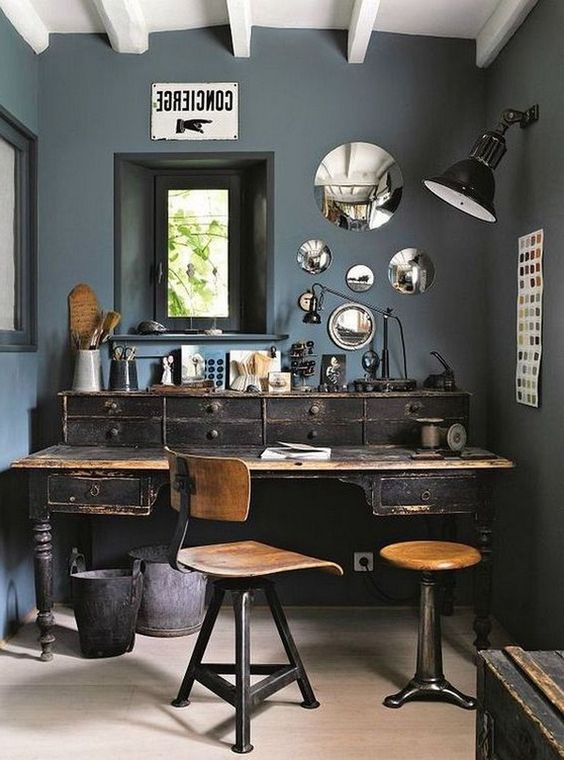 an industrial home office with grey walls, an arrangement of mirrors, a shabby chic wooden desk and industrial chairs
