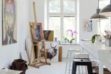 a Nordic art studio with a large white table, a row of stools, an easel, some bright artwork, potted plants and blooms