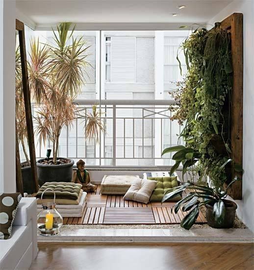 a balcony turned into a meditation space with cushions and rugs plus a lush greenery wall