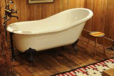 a barn bathroom fully decorated with wood, with a clawfoot tub, a bright rug and vintage fixtures and appliances