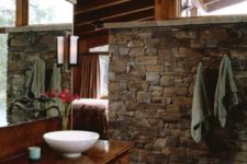 a barn bathroom with a stone wall, stained wood everywhere and a large mirror plus a bowl sink