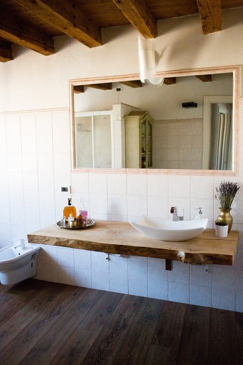 A barn bathroom with a wooden ceiling with beams, white tiles, a wall mounted wooden vanity and a large mirror