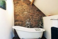 a barn bathroom with white walls and a ceiling, wooden beams, a stone wall, a clawfoot tub and an artwork