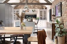 a barn kitchen with white cabinets, wooden beams, a white kitchen island, metal pendant lamps and artwork