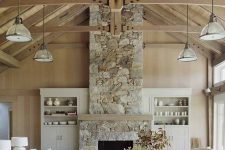 a barn living room with stained walls and a ceiling, with wooden beams, a fireplace clad with stone, neutral seating furniture and built-in storage units