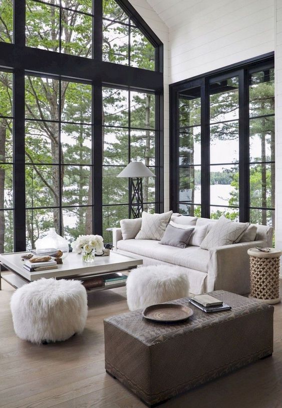 A beautiful barn living room with double height windows, neutral furniture and a brown ottoman, faux fur stools is amazing