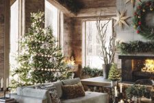 a beautiful barn living room with wooden walls, a ceiling and wooden beams, a fireplace clad with concrete, a low sectional, a wooden bench, a Christmas tree and arrangements