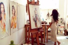 a boho home artist studio with stained wooden furniture and an easel, a metal storage shelf, baskets with lids and lots of art